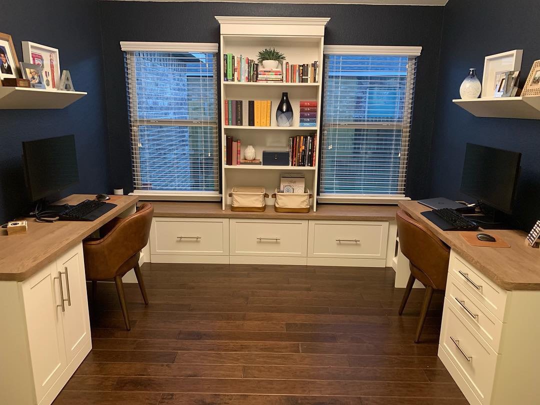 Second view of the home office space for two, with two white desks, bookshelves and storage