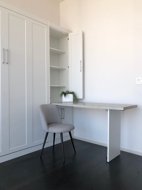 A drop-down desk folds out of a tall white cabinet, providing a convenient home office setup