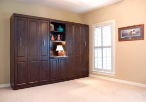 Tall dark wood cabinets hide a Murphy bed near a set of windows 