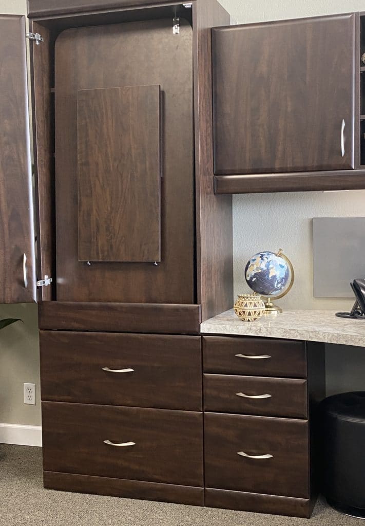 A drop-down desk is folded away into a dark wood cabinet, leaving more space available within the home office 