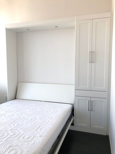 Tall white cabinets open to reveal a white Murphy bed, made up and ready for guests