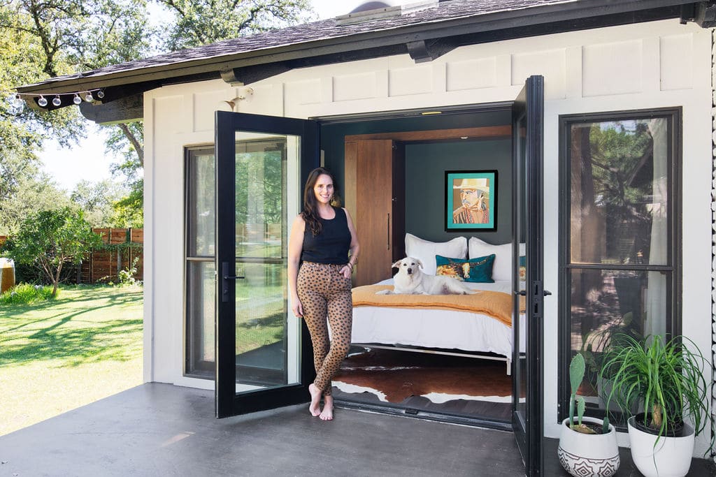 Interior designer stands in front of open double door, showcasing a stylish murphy bed in Austin, Texas.