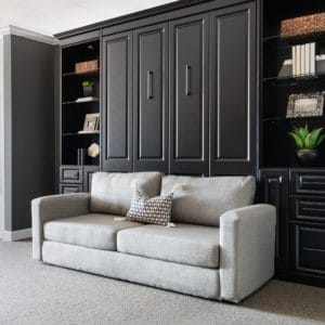 Sophisticated space saving Murphy bed closed behind modern custom black wooden cabinets.