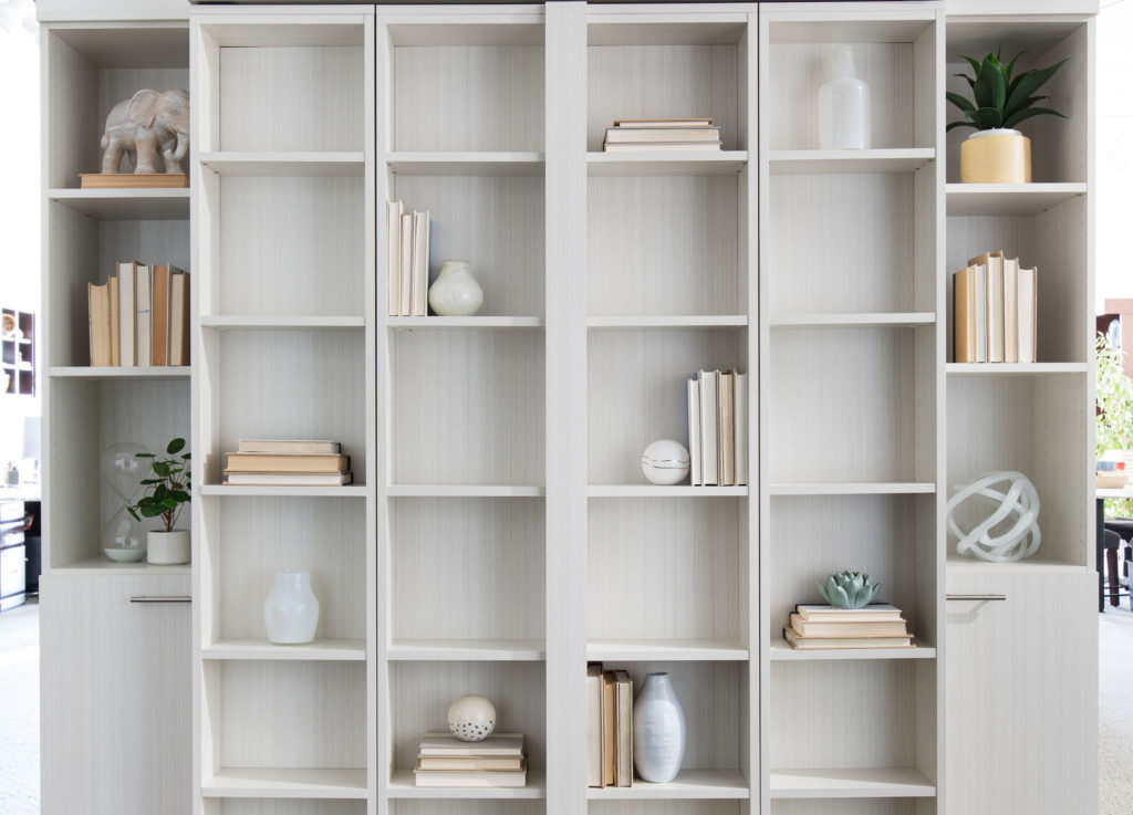Six tall light gray bookshelves with square cubicles, some bare, others featuring books, neutral vases, elephant figurine, plants and sculptures.