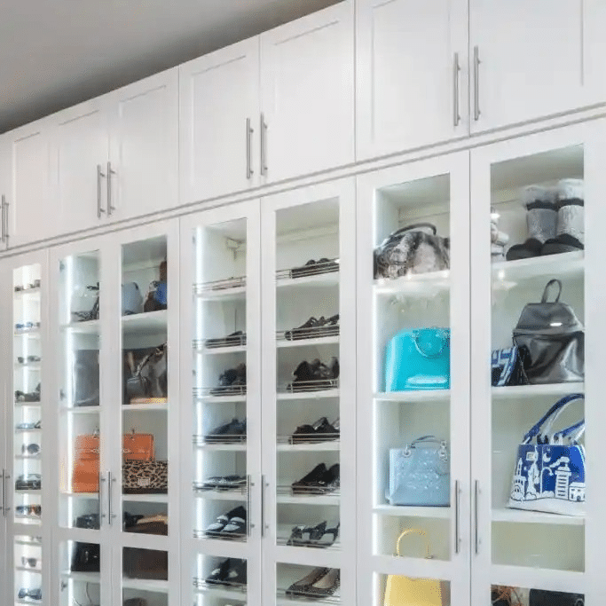 White shaker closet in a floor to ceiling solution with lighted cabinets with glass doors.