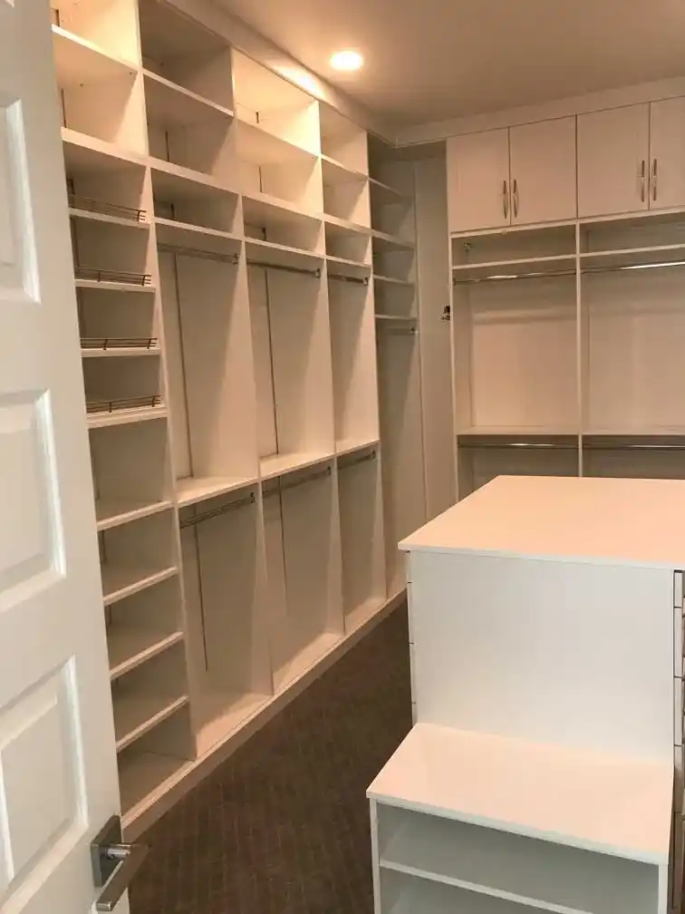 Floor to ceiling white shaker walk-in closet with island.