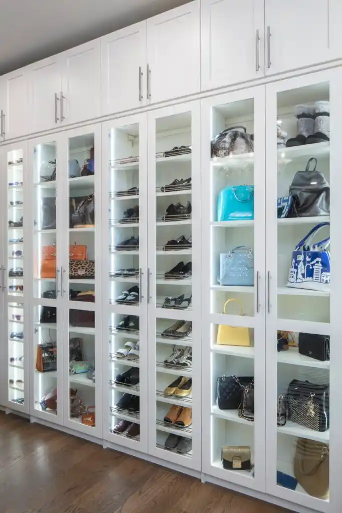 White shaker closet in a floor to ceiling solution with lighted cabinets with glass doors.